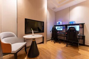 A hotel room with a flat-screen TV, a gaming chair, a small round table, and a desk with multiple monitors. - Heyiyuezhi S Hotel (Dongguan Fenggang Town People's Hospital Yongsheng Street) (Dongguan)