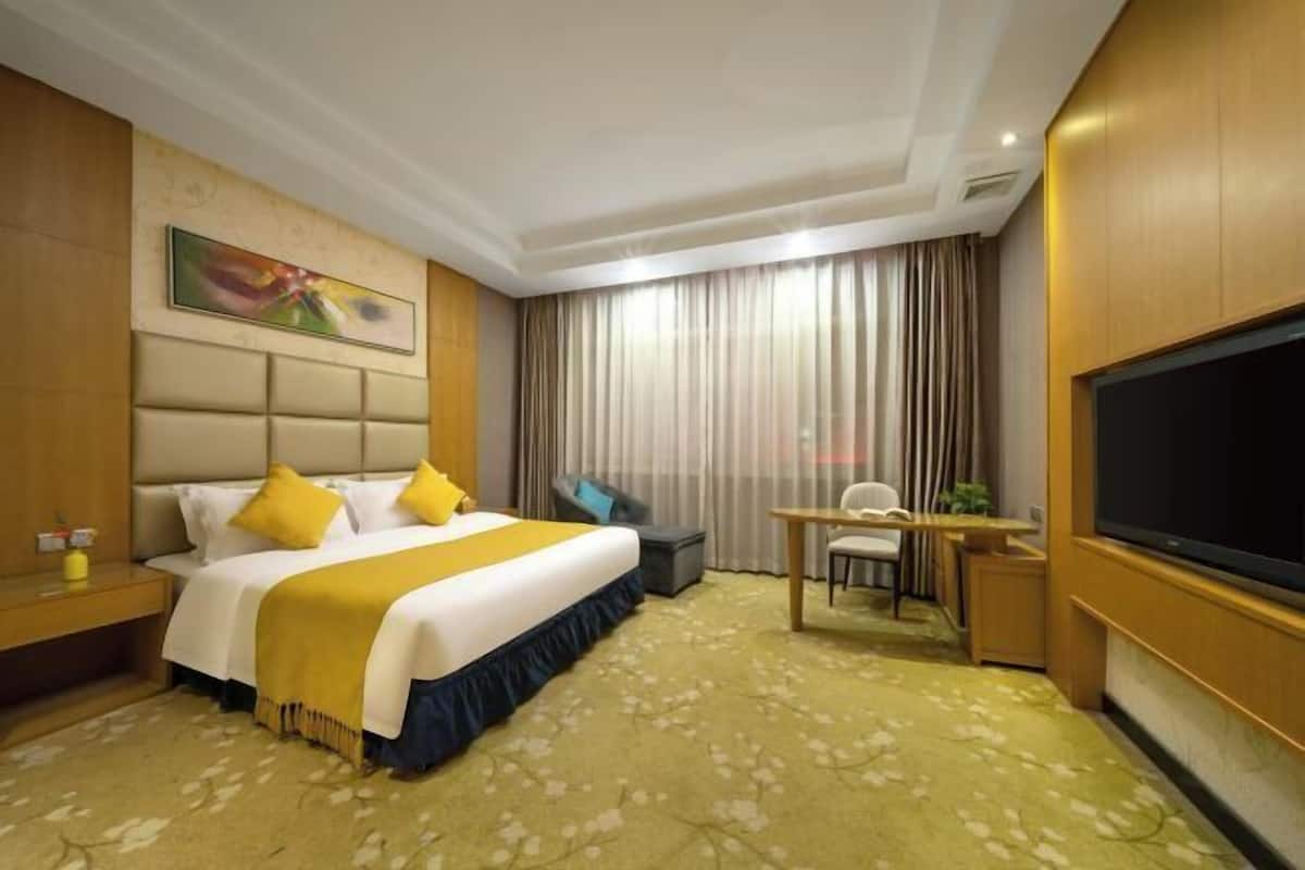 A hotel room with a bed, desk, chair, TV, and curtains.