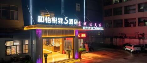A hotel with a neon sign, a wet ground, and a parked car.