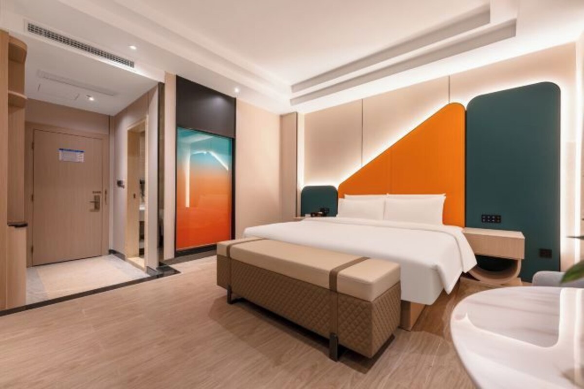 A modern hotel room with a large bed, a bench, a bedside table, and a nightstand.