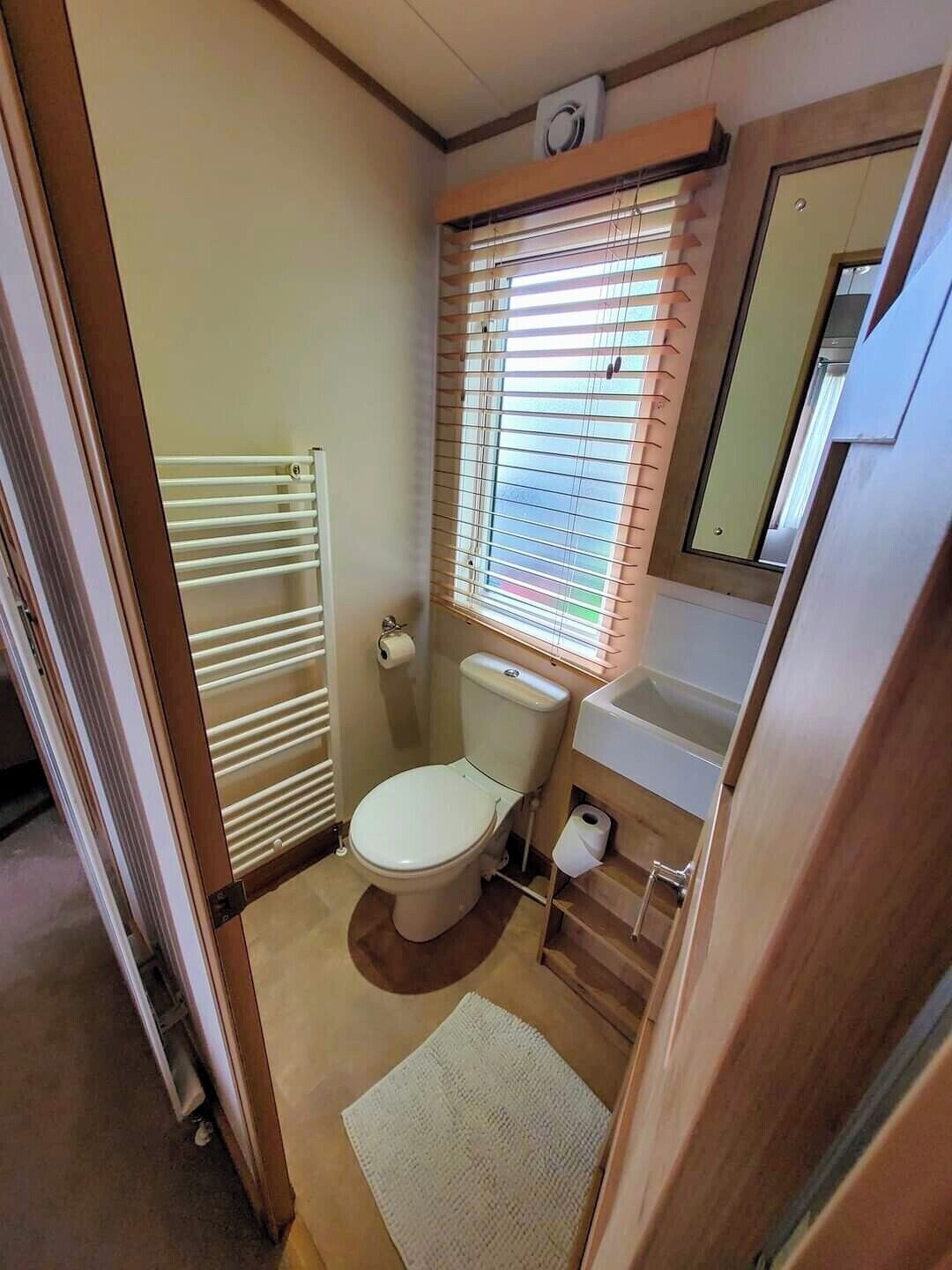 A compact bathroom with a toilet, sink, and window with blinds.