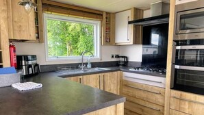 A modern kitchen with wooden cabinets, a large window, a gas stove, and built-in appliances. - The Westwood at Percy Wood (Morpeth)