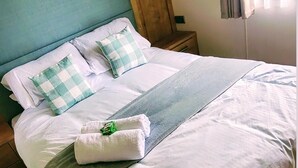 A neatly made bed with white linens and checkered pillows, a grey blanket, and a folded towel with a green tag. - The Westwood at Percy Wood (Morpeth)
