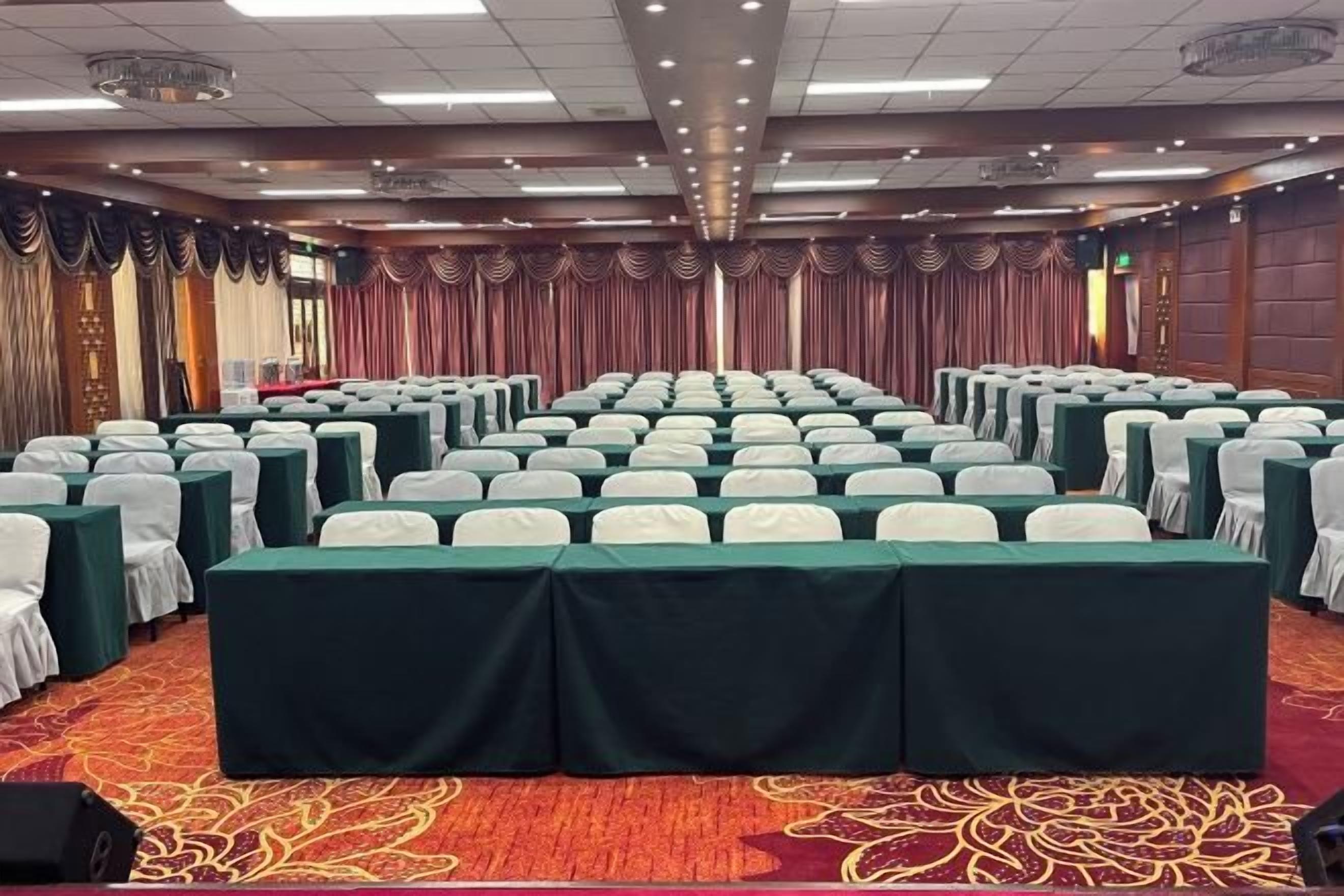 A conference room with rows of tables and chairs, a carpeted floor, and a draped curtain backdrop.
