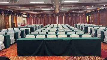 Un salón de conferencias con filas de mesas y sillas, piso alfombrado y un telón de fondo con cortinas.