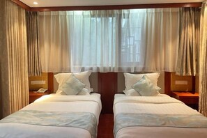 Een hotelkamer met twee bedden, een nachtkastje met een telefoon en dunne gordijnen.