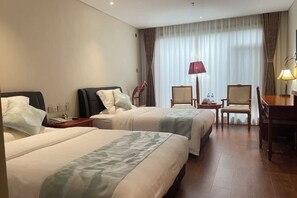 Een hotelkamer met twee bedden, een bureau, een stoel, een lamp en een raam met gordijnen.