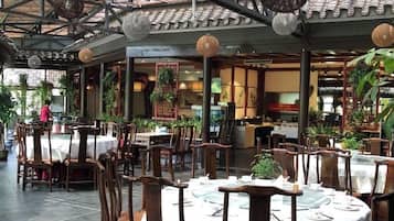 Un comedor interior con mesas y sillas, un techo con luces colgantes y plantas en macetas.