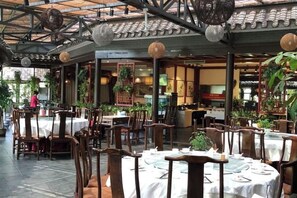 An indoor dining area with tables and chairs, a ceiling with hanging lights, and potted plants. - Oriental Zeng Hotel (Beijing)
