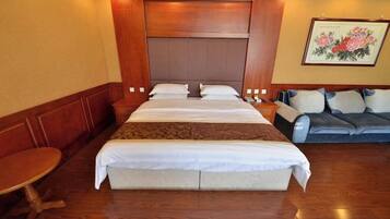 A hotel room with a large bed, a sofa, a small table, and a painting on the wall.