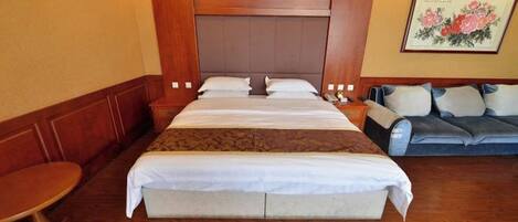 Habitación de hotel con una cama grande, un sofá, una mesita y un cuadro en la pared.