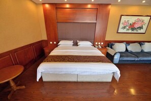 Een hotelkamer met een groot bed, een bank, een kleine tafel en een schilderij aan de muur.