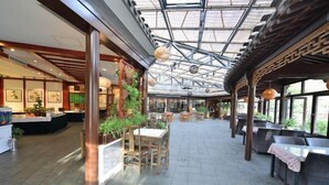 An indoor dining area with wooden tables and chairs, a glass ceiling, and potted plants. - Oriental Zeng Hotel (Beijing)