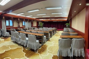 A conference room with rows of tables and chairs, a stage, and a carpeted floor.