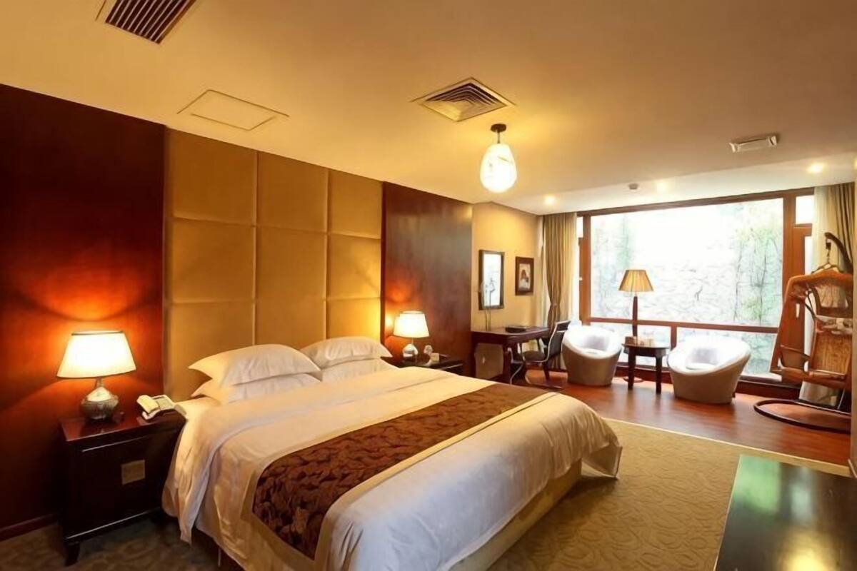 Une chambre d’hôtel avec un grand lit, des lampes de chevet, un bureau, une chaise et une vue sur l’extérieur.