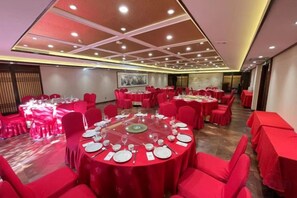 Een feestzaal met ronde tafels gedekt voor een diner, rode stoelen en een modern plafondontwerp.