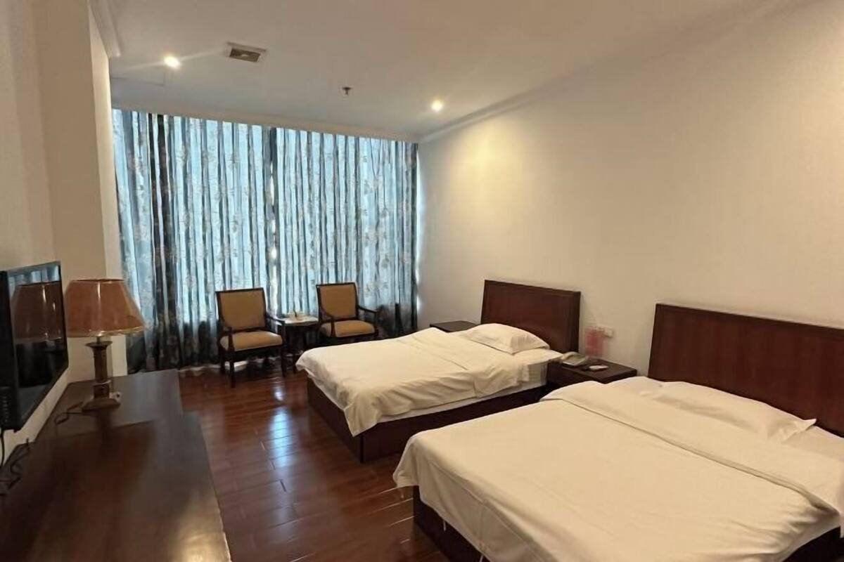 Ein Hotelzimmer mit zwei Betten, einem Schreibtisch, einem Stuhl und einem großen Fenster mit Vorhängen.