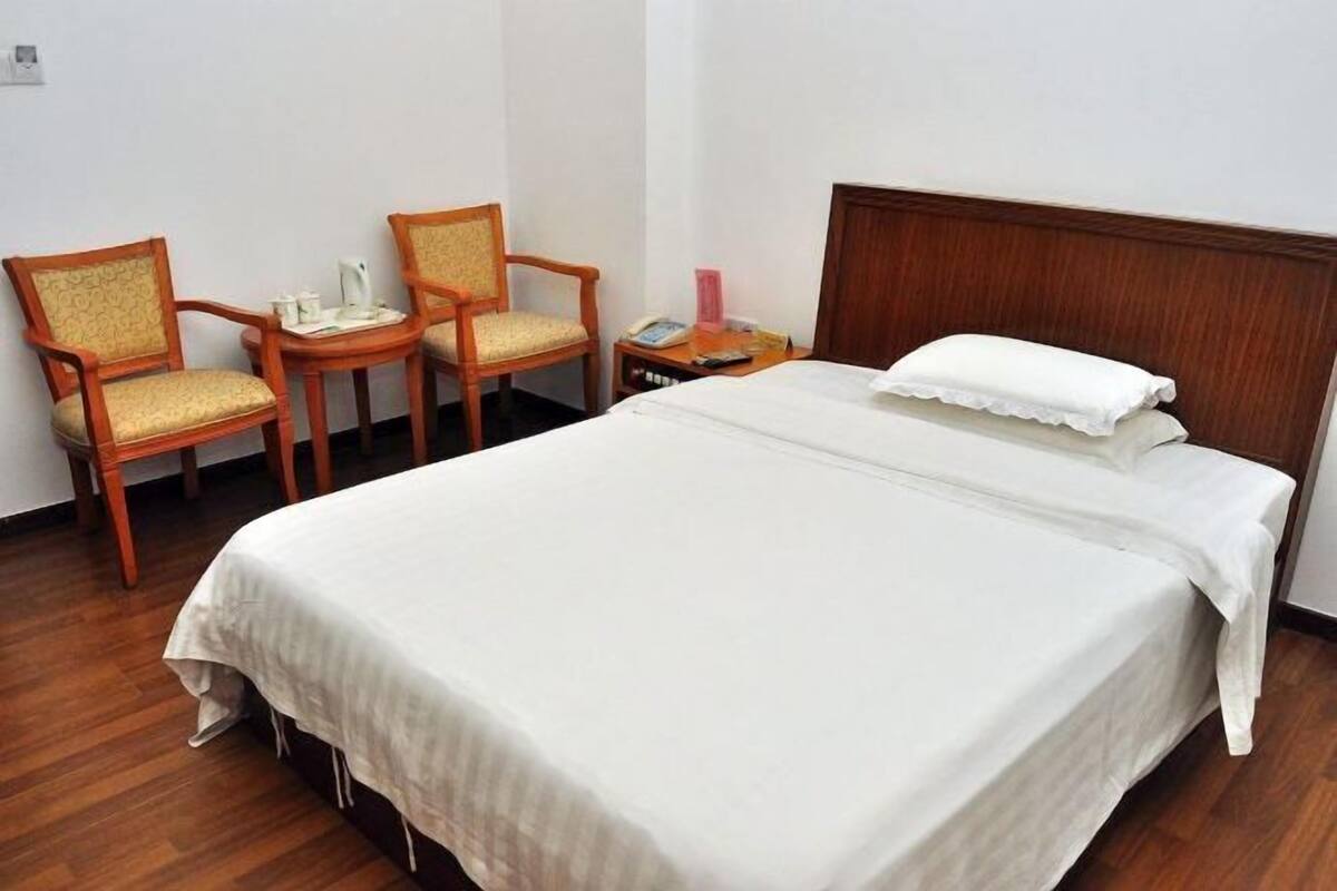 Ein ordentlich eingerichtetes Hotelzimmer mit einem großen Bett, zwei Stühlen, einem kleinen Tisch und einem Nachttisch.
