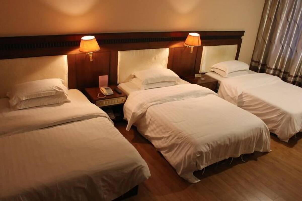Ein Hotelzimmer mit drei Einzelbetten, Holzkopfteilen, Nachttischlampen und einem Telefon auf dem Nachttisch.