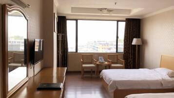 Habitación de hotel con dos camas, un escritorio con silla, televisión y un amplio ventanal con cortinas.