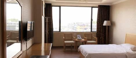 A hotel room with two beds, a desk with a chair, a TV, and a large window with curtains.