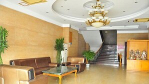 Un hall d’entrée spacieux avec un plafond incurvé, un lustre, des canapés en cuir, une table basse et un escalier menant à l’étage supérieur.