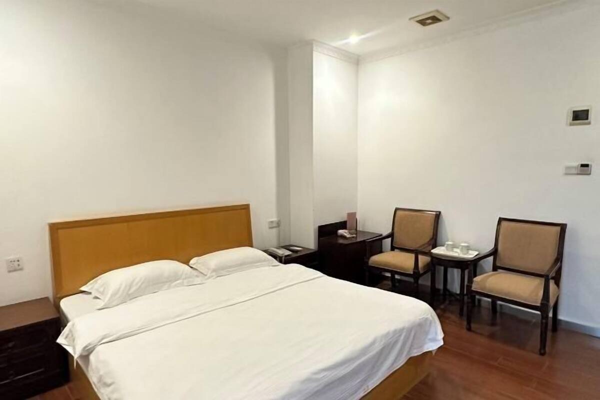 Ein Hotelzimmer mit einem Bett, zwei Stühlen, einem kleinen Tisch und einem Nachttisch.