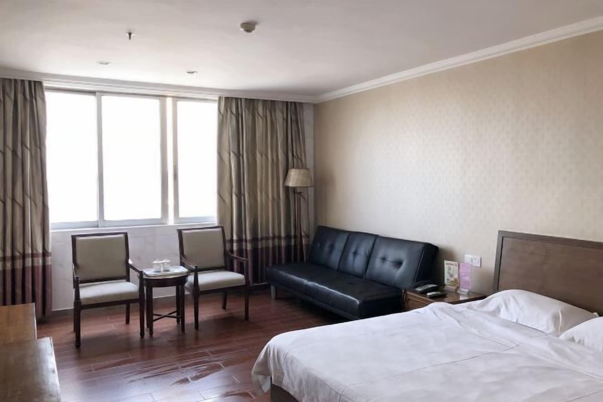Une chambre d’hôtel comprenant un lit, un canapé, deux fauteuils, une petite table, une lampe et une table de chevet avec un téléphone.