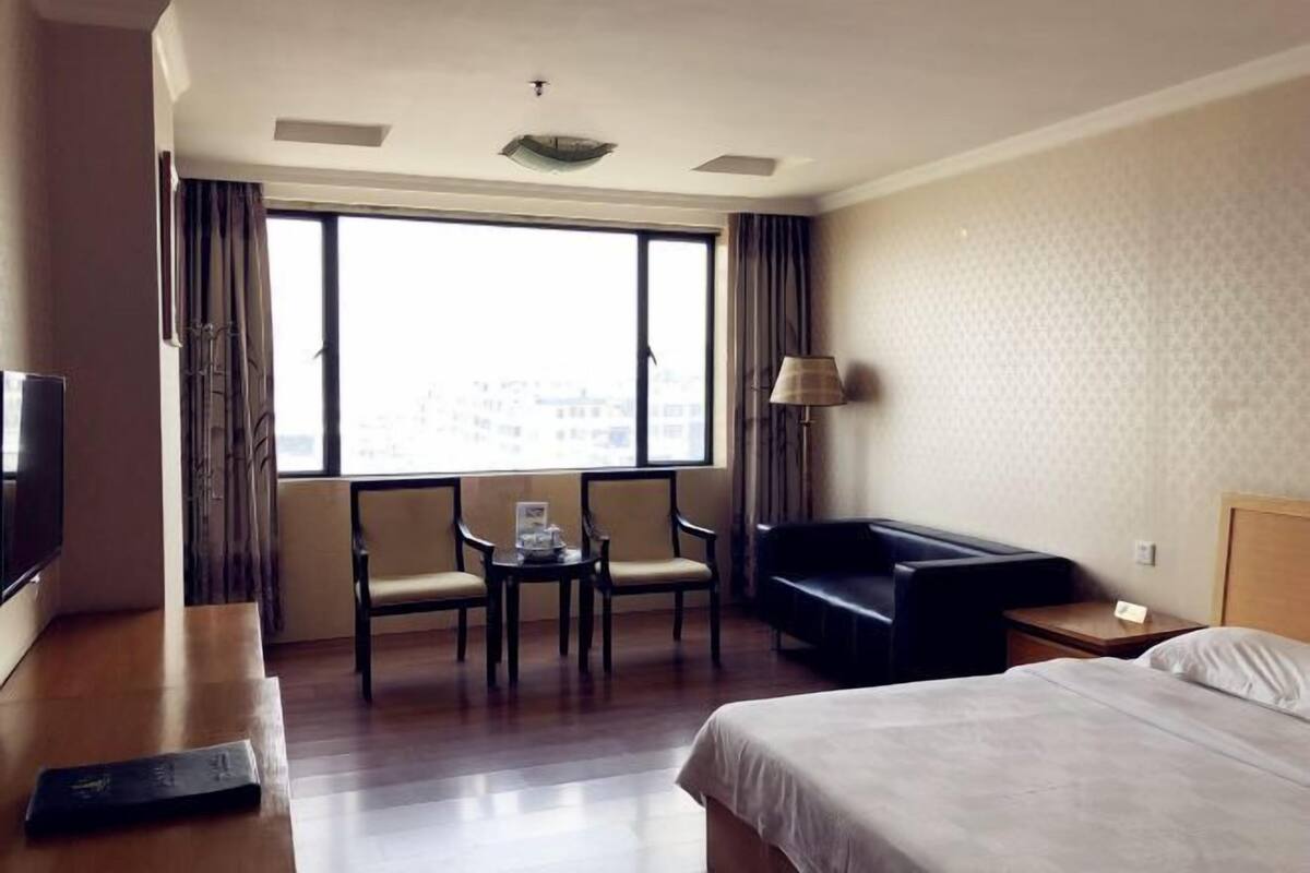 Ein Hotelzimmer mit Bett, Schreibtisch, Fernseher, Sofa und einem Fenster mit Vorhängen.