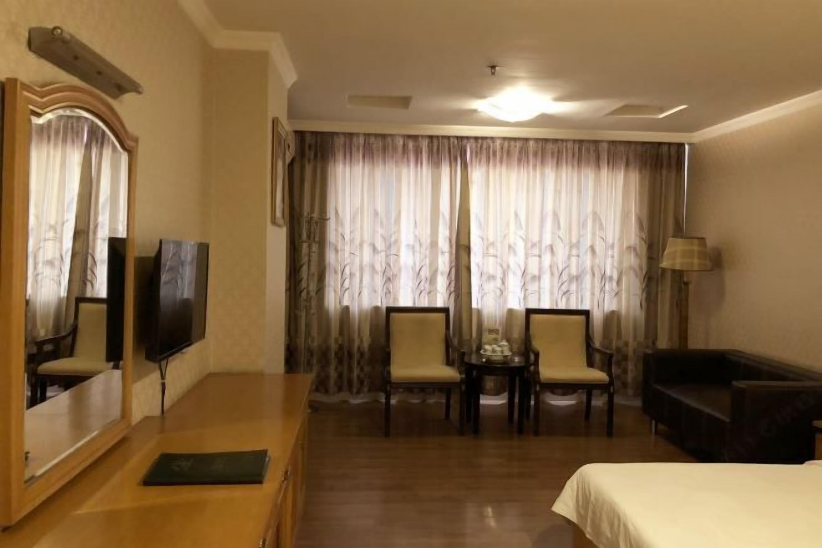Habitación de hotel con cama, televisión, escritorio con silla, una mesita con dos sillas y un sofá.
