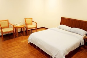 Une chambre d’hôtel avec un lit en bois, deux chaises, une petite table avec un plateau, et un mur blanc.