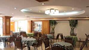 Un espace repas avec des tables et des chaises rondes, un lustre et des plantes en pot.
