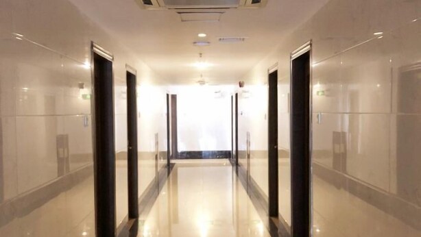 Un couloir d’hôtel moderne, avec des portes en verre, un sol brillant et un plafond doté d’un éclairage encastré.