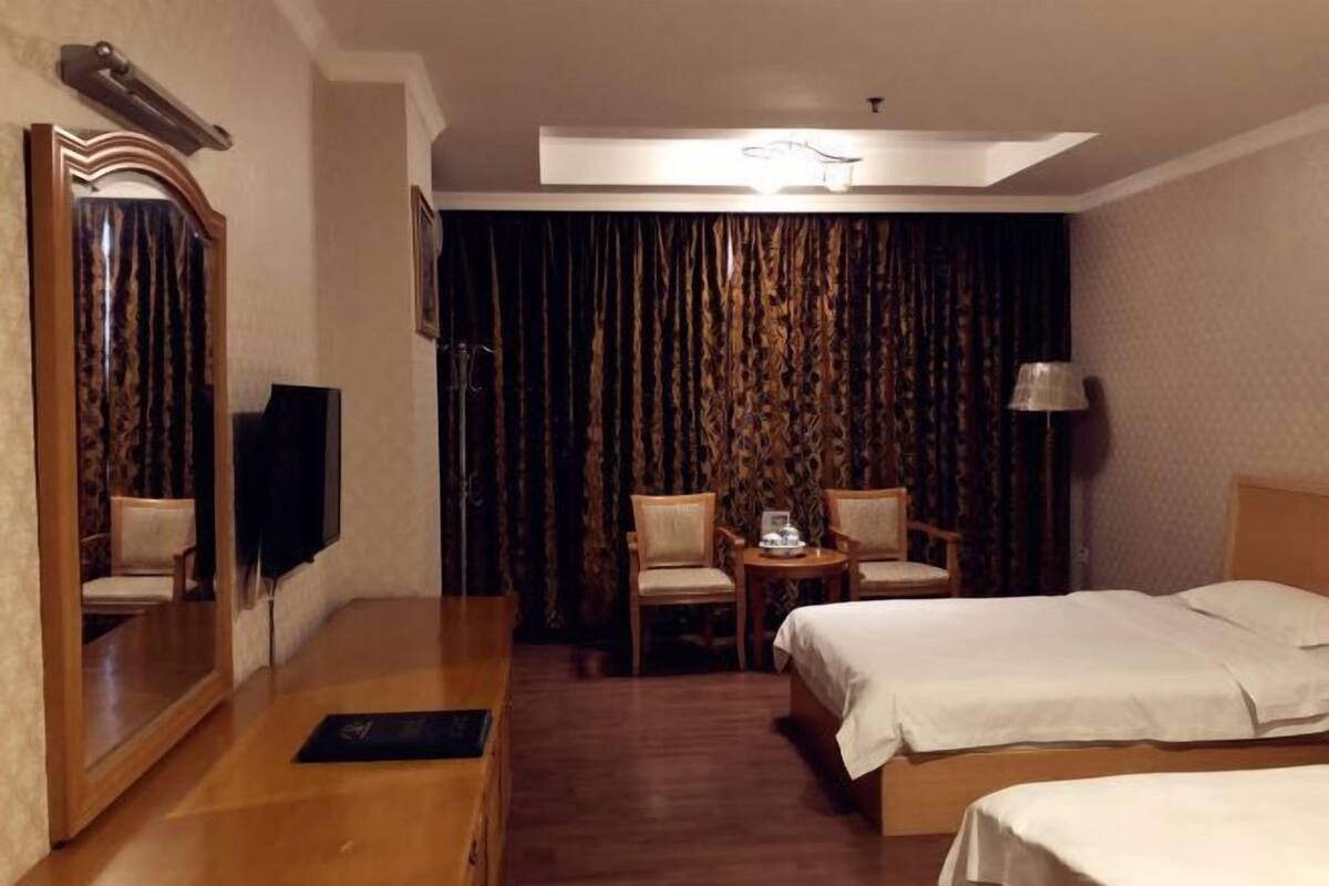 Ein Hotelzimmer mit Bett, Schreibtisch, Stuhl, kleinem Tisch mit Lampe und großem Spiegel.