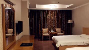 Habitación de hotel con cama, escritorio, silla, pequeña mesa con lámpara y un espejo grande.