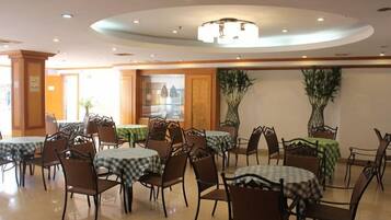 A dining area with multiple tables and chairs, a central chandelier, and potted plants.