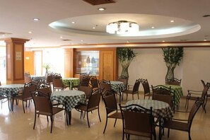 A dining area with multiple tables and chairs, a central chandelier, and potted plants. - Yijing Hotel (Guangzhou)