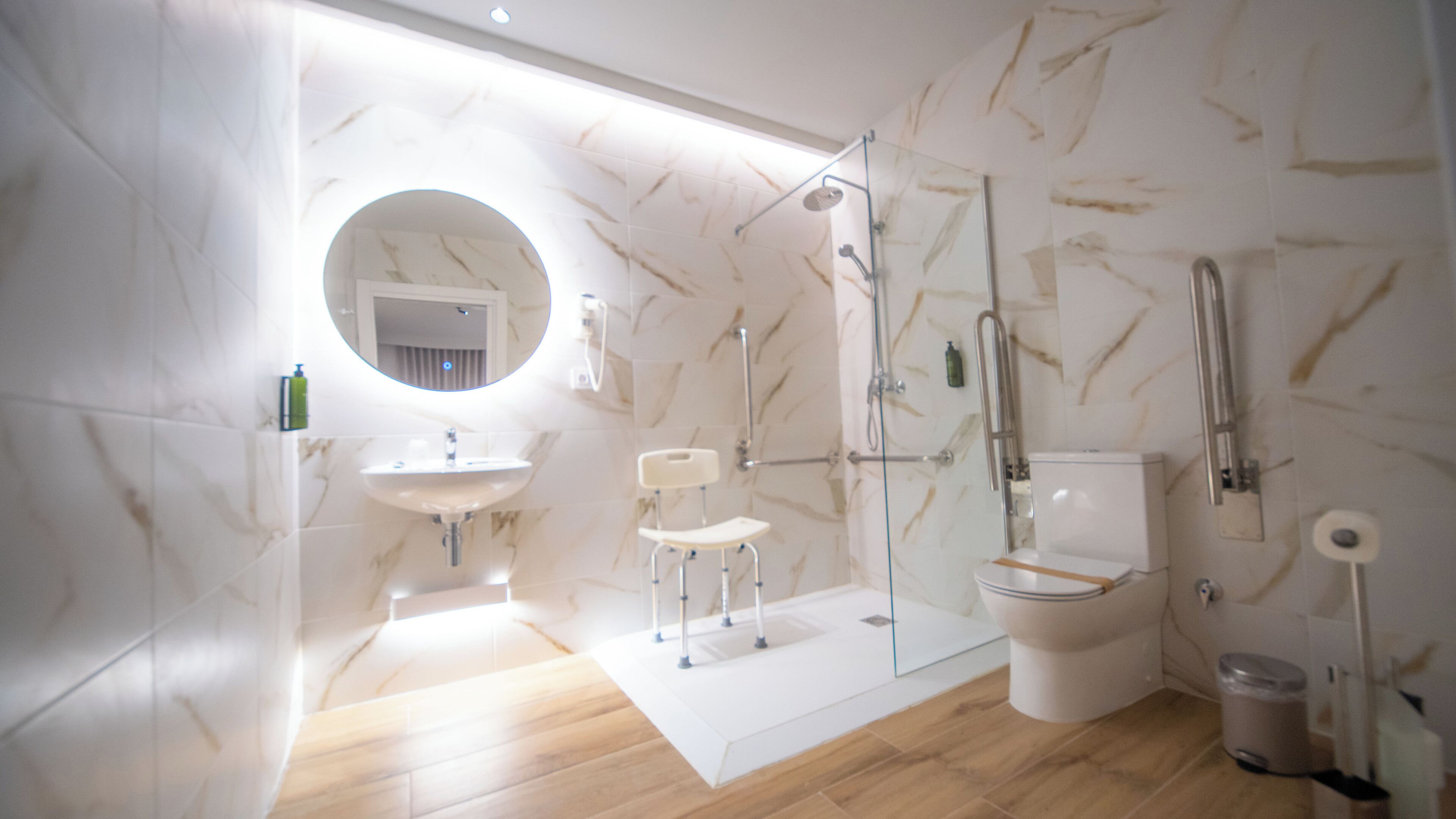 A modern bathroom with a marble floor, a round mirror, a sink, a toilet, and a glass-enclosed shower area.