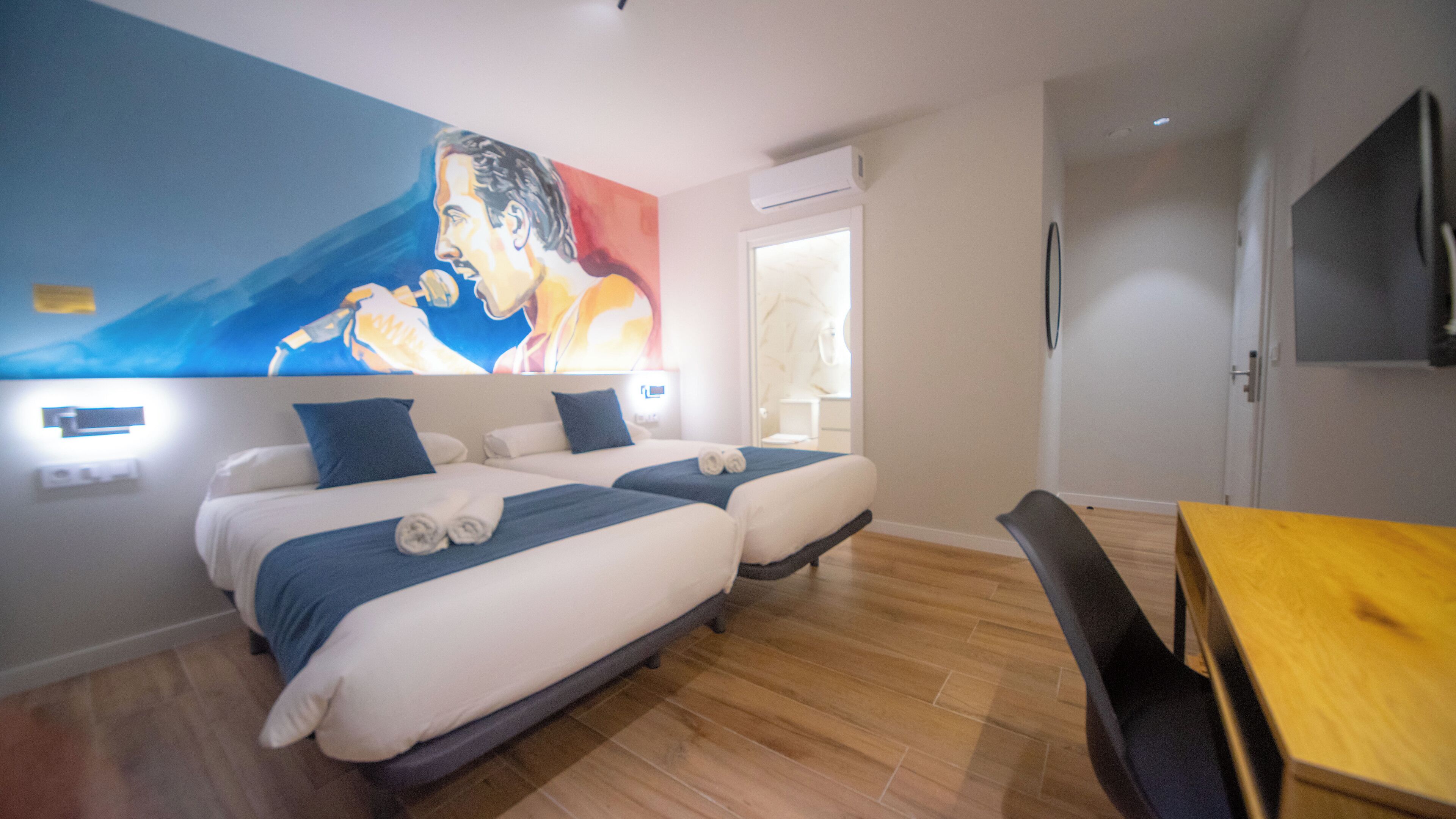 Habitación de hotel con dos camas, suelo de madera, un cuadro en la pared y un televisor.