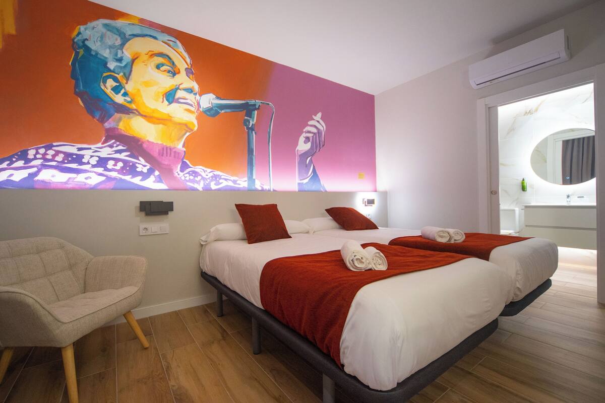 A hotel room with a bed, a chair, a painting, and a bathroom visible through an open door.