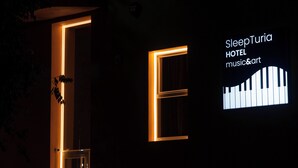 Une entrée d’immeuble avec des encadrements de porte illuminés et une enseigne indiquant « SleepTuria Hotel, musique et art ».