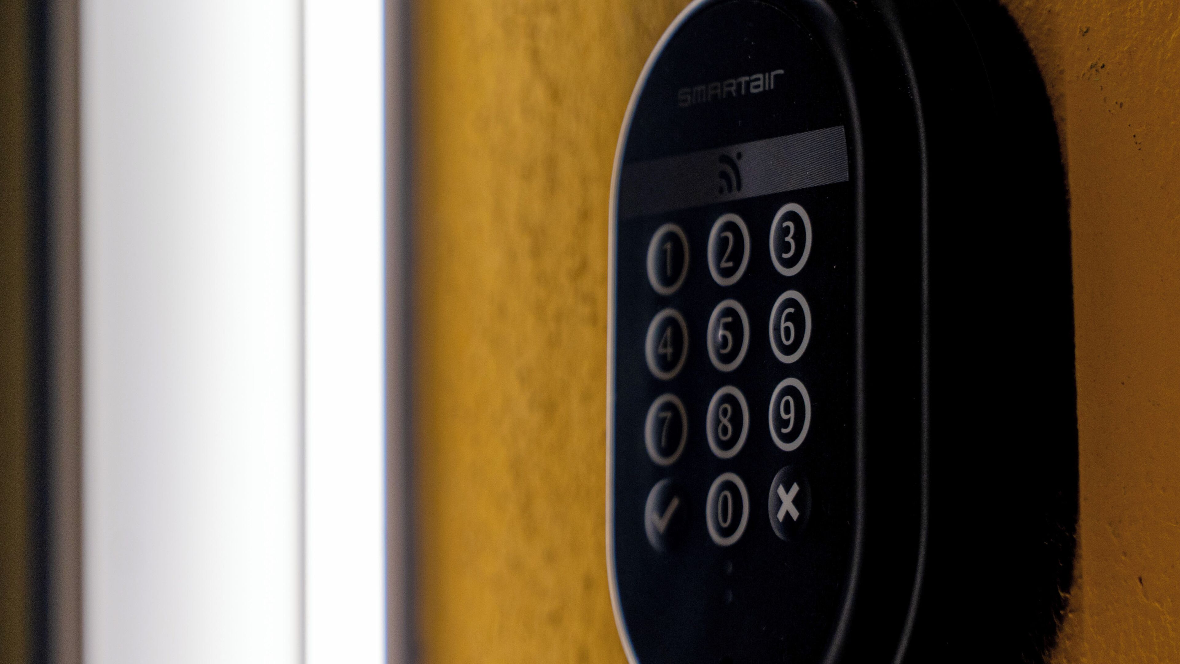 A black intercom with a numeric keypad and a speaker grille, mounted on a wooden surface.