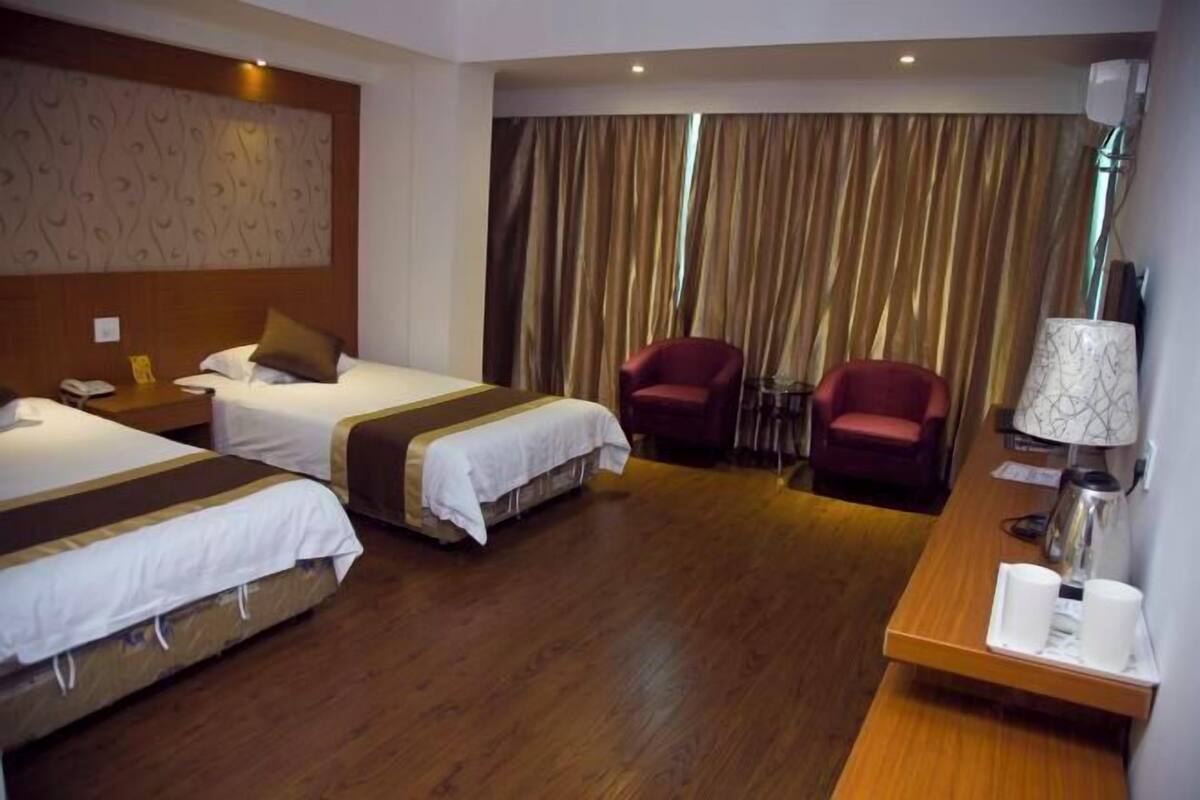 A hotel room with two beds, a desk with a lamp, a chair, and a curtain backdrop.