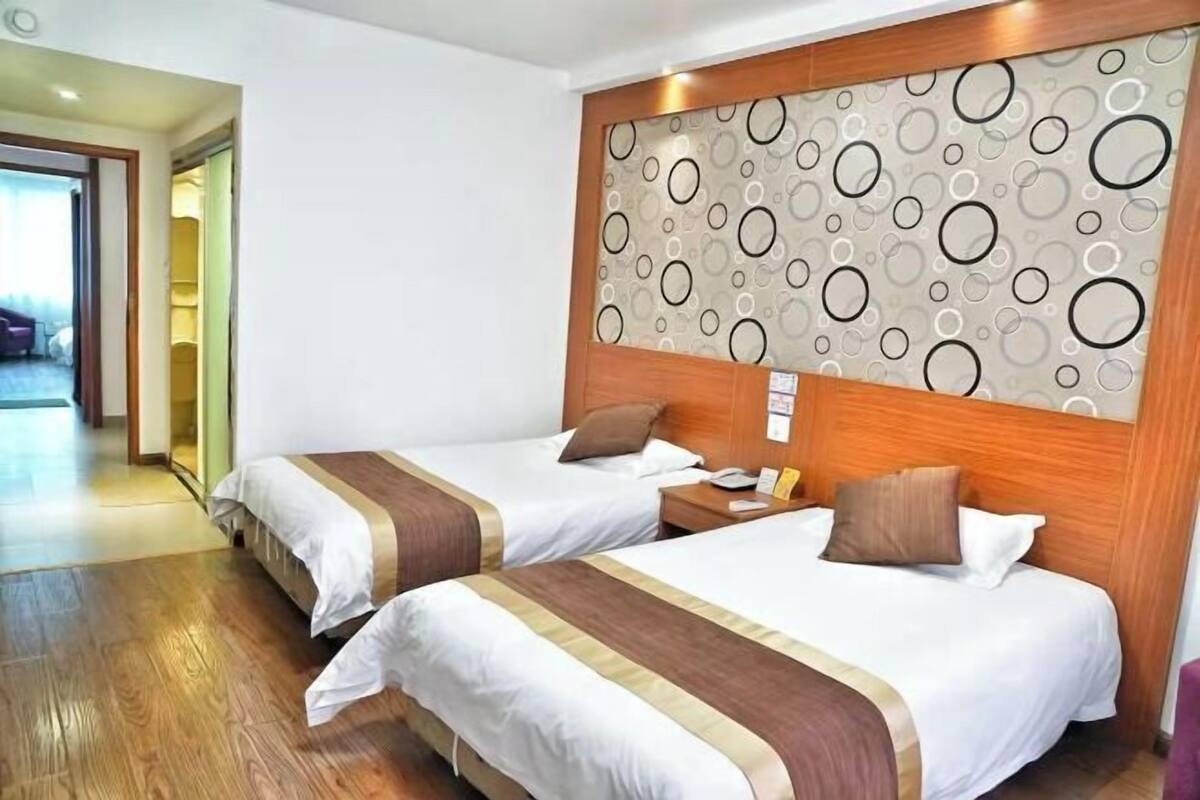 A hotel room with two beds, wooden headboards, a patterned wall, and a wooden floor.