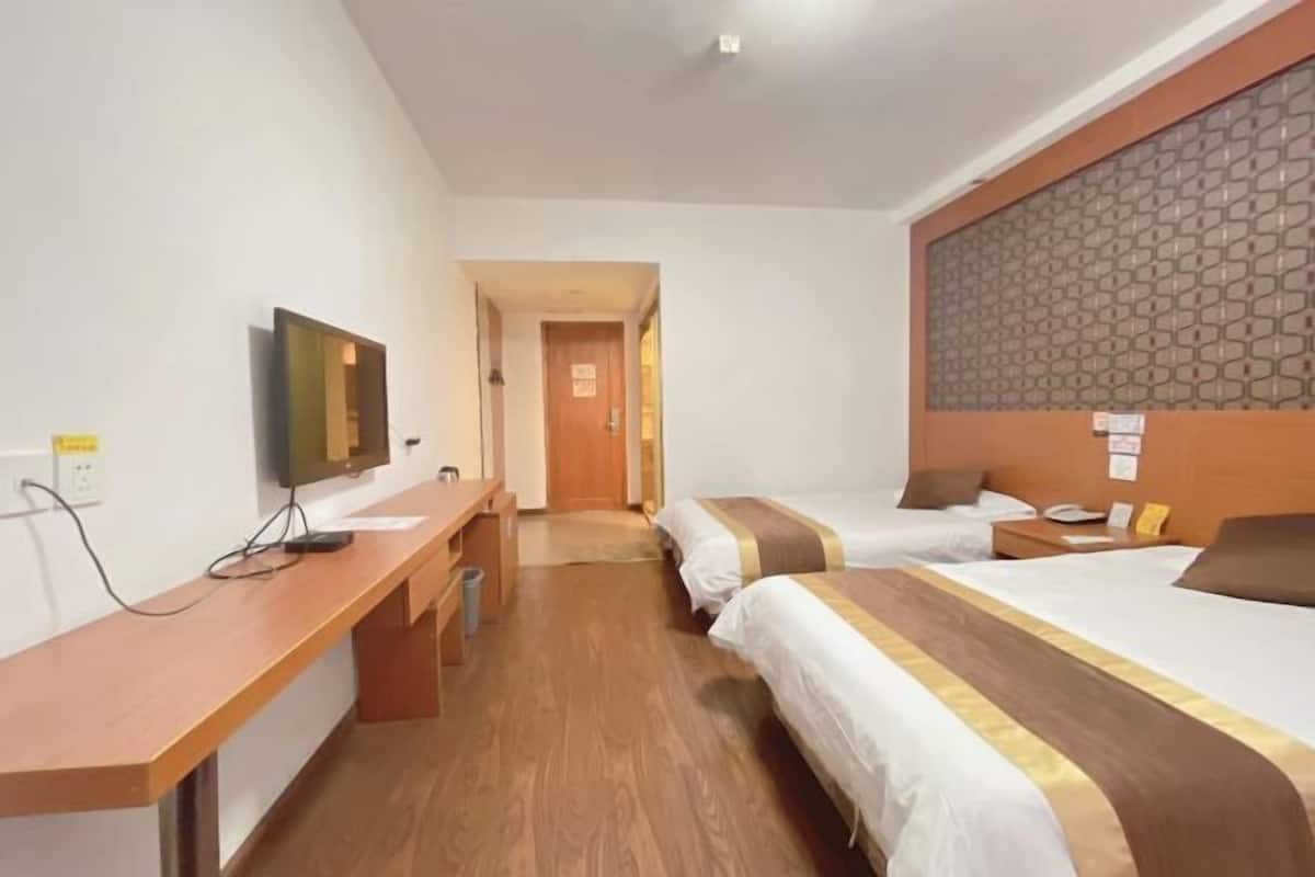 A hotel room with two beds, a desk, a TV, and a patterned headboard.