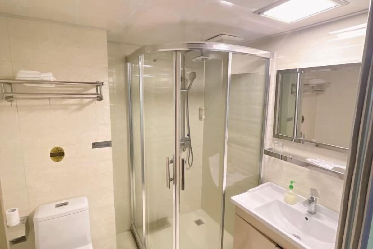 Une salle de bain moderne avec une douche à l’italienne, un lavabo blanc avec un miroir au-dessus, et des toilettes sur la gauche.
