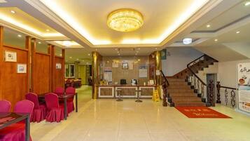 Un vestíbulo de hotel con una recepción, una escalera y un área de descanso con mesas y sillas.