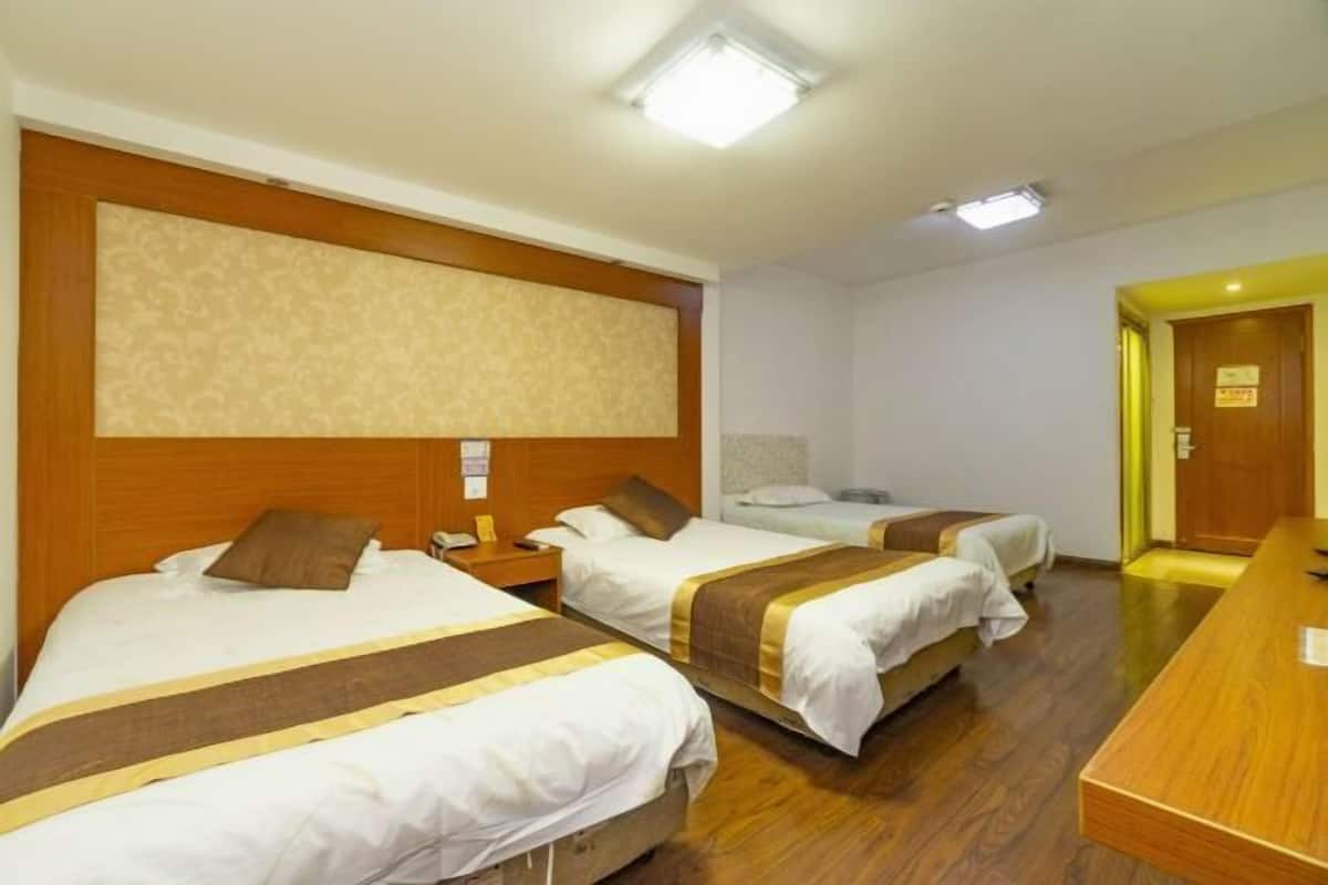 A hotel room with three single beds, a wooden headboard, a desk, and a door with a sign.
