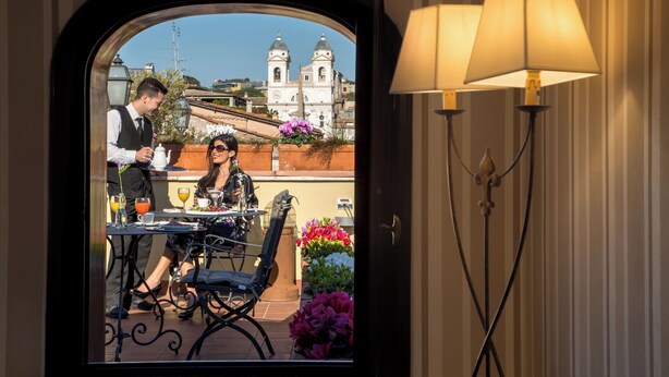 A dining area with a view of a historic building, a table with chairs, and a lamp. - The Inn at the Spanish Steps Exclusive Collection - Condotti Luxury Suites (Rome)