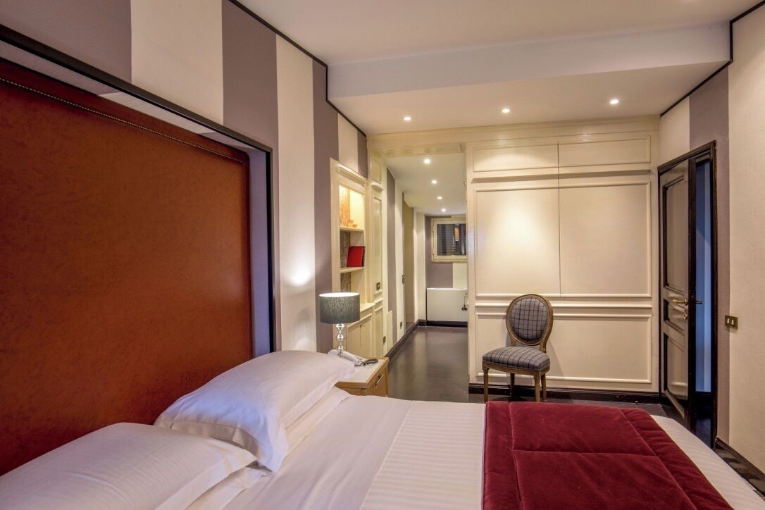 A hotel room with a large bed, a desk with a chair, and a wardrobe.